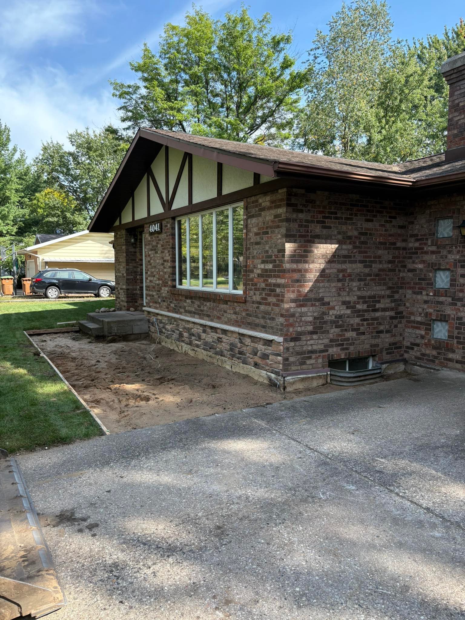 Residential brick house exterior with landscaped yard and unfinished front area.