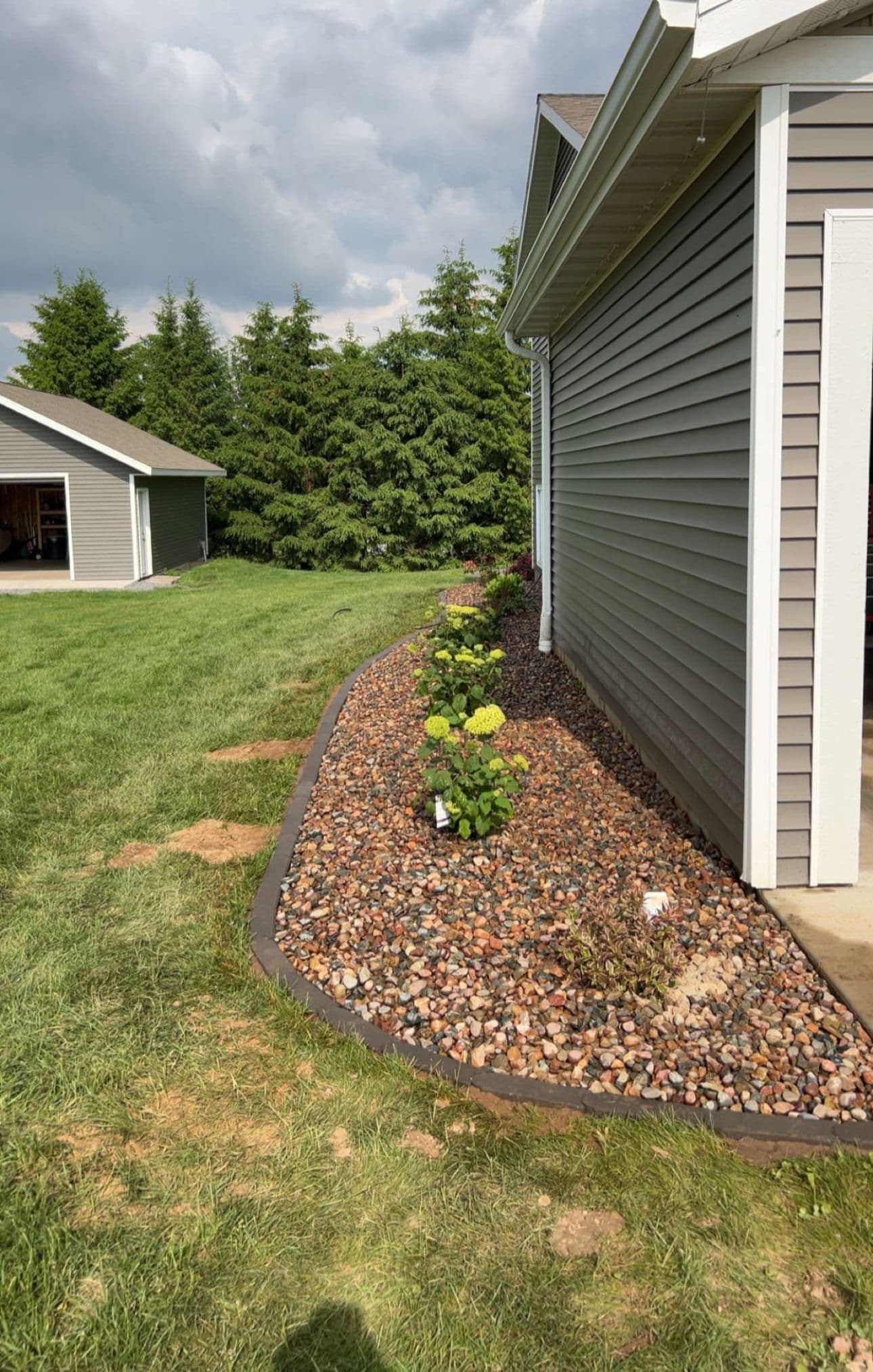 Landscaped garden bed with colorful flowers and stone border next to a house.